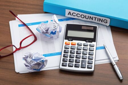 Calculator with accounting sheets and crumpled paper on wooden office desk. Business financial trouble conceptの写真素材