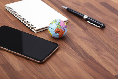 Smart phone with world map and notebook on wooden office desk