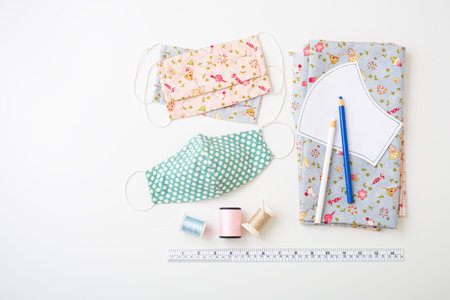 Homemade cotton face mask with fabric, pattern, threads on white background, flat lay