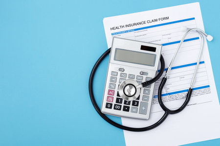 Health insurance claim form with stethoscope and surgical mask, top view