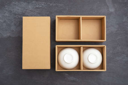 Ceramic bowl in paper gift box package mockup on black stone background, top view with copy spaceの写真素材