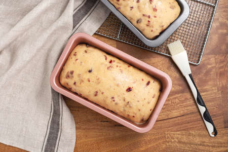 Bread dough with cranberry in pink loaf pan on wooden table, top viewの写真素材