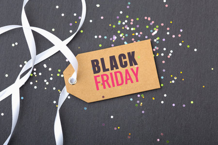 Black friday sale tag with white ribbon and glitter on dark stone background