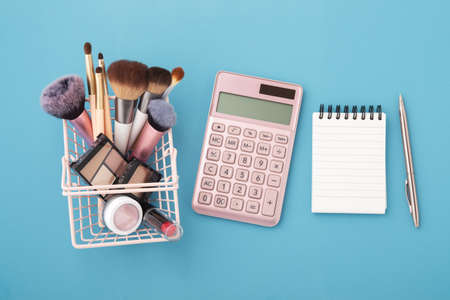 Makeup beauty products with pink calculator and notebook on blue background, top viewの写真素材
