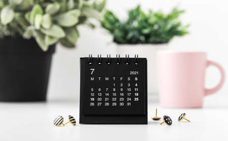 Black calendar with pins and green plants on white tableの写真素材