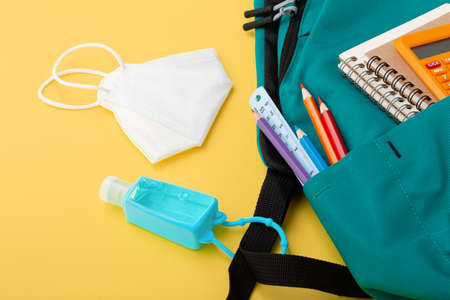 Backpack with protective face mask and hand sanitizer gel on yellow backgroundの写真素材