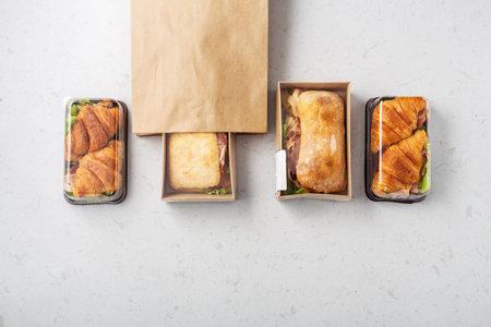 Sandwich with ciabatta and croissant in takeout or delivery food container on marble table, takeaway meal, top viewの写真素材