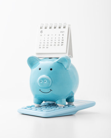 Blue piggy bank on calculator with calendar on white backgroundの写真素材