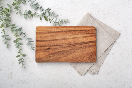 Wood cutting board with linen napkin and plant  on marble table, top view