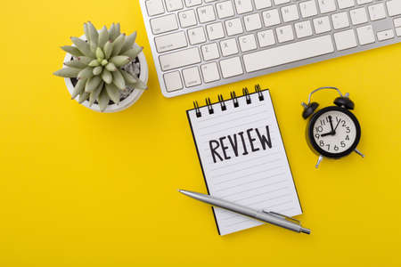 Review word on notebook with computer keyboard and clock on yellow background, top viewの写真素材