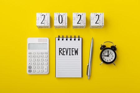 Review word on notebook with 2022 wood block and calculator on yellow background, financial review conceptの写真素材
