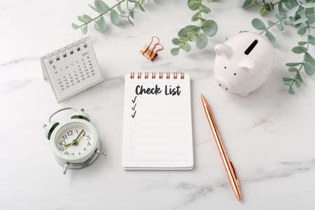 Checklist with calendar and piggy bank on marble table with plantの写真素材