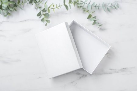 Open white box mockup on marble table with plant, top view