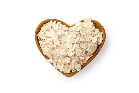 Rolled oat flake in heart wooden bowl isolated on white backgroundの写真素材