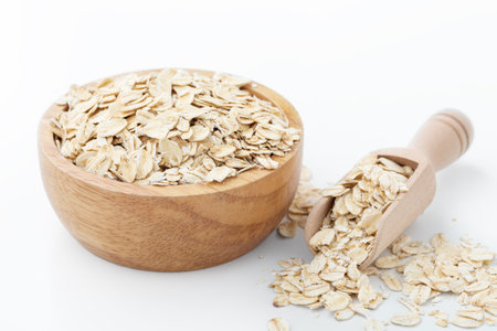 Rolled oat, raw oatmeal in wooden bowl with scoop on white background