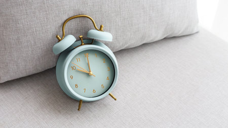Pastel blue vintage alarm clock on fabric cozy couch backgroundの写真素材