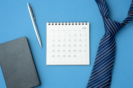 Calendar 2023 with tie, notebook and pen on blue background, business meeting, scheduling or planning, top viewの写真素材