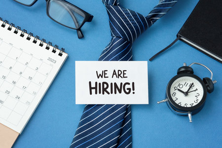 Job recruitment concept, we are hiring sign with tie, calendar and clock on office tableの写真素材