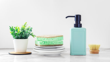 Cleaning sponge on plates with green dish soap bottle and washing brushes on white marble kitchen tableの写真素材
