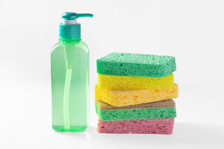 Green liquid dish washing detergent with stack of sponges on white backgroundの写真素材