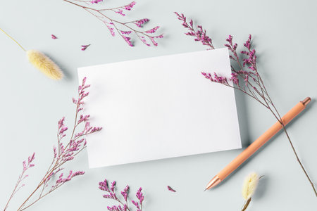 White card with pen and pink flower on pastel light green background, top viewの写真素材