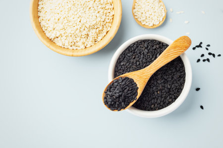 Black sesame in white bowl with wood spoon and white sesame on blue background, top view, copy spaceの写真素材