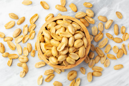 Roasted peanuts in wooden bowl on marble table, top view