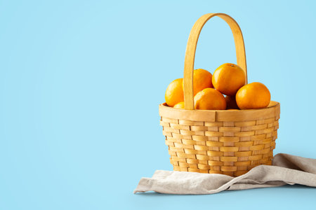 Oranges fruit in woven basket on linen fabric on blue background, copy spaceの写真素材