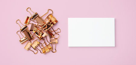 Rose gold binder clips and memo note paper on pastel pink background, top viewの写真素材