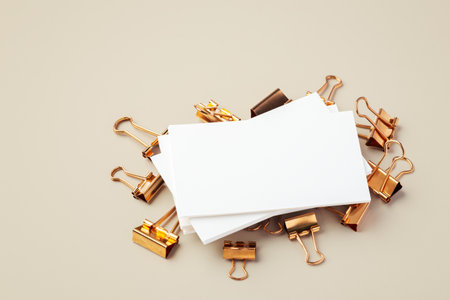 Blank business card on gold binder clips on light beige background, copy spaceの写真素材