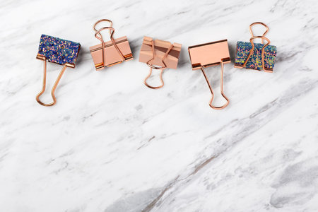 Rose gold binder paper clips on white marble table background, top view, copy spaceの写真素材