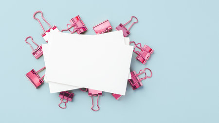 Blank business card mockup on pink binder clips on light blue background, top view, copy spaceの写真素材