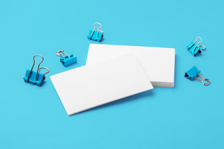 Blank business card, mockup with paper binder clips on blue backgroundの写真素材