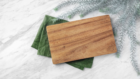 Wooden plate on green linen napkin on marble table with leaves, top viewの写真素材