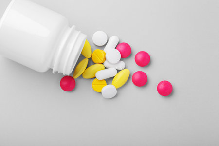 Medical pills, tablet, drugs spilling out of white medicine bottle on grey background, top viewの写真素材