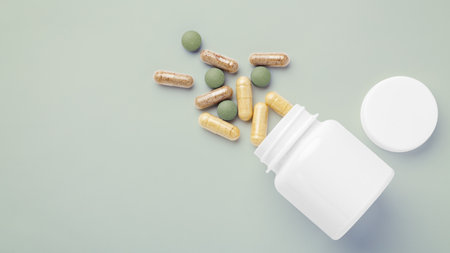 Natural supplement, vitamin spilling out of medical bottle on green background, top view, copy spaceの写真素材