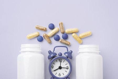 Supplement tablet, beauty vitamin capsule with white bottle and alarm clock on pastel purple background, top view, copy spaceの写真素材