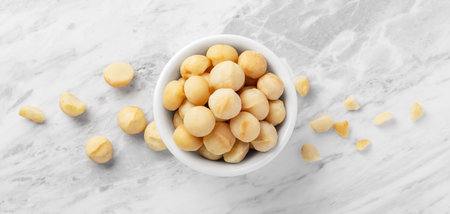 Macadamia nuts in white bowl on marble table background, top viewの写真素材