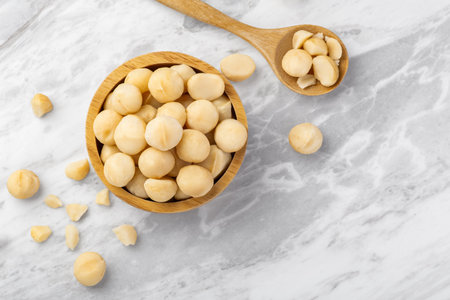 Macadamia nuts in wooden bowl with spoon and cracked macadamia on marble table background, top view, copy spaceの写真素材