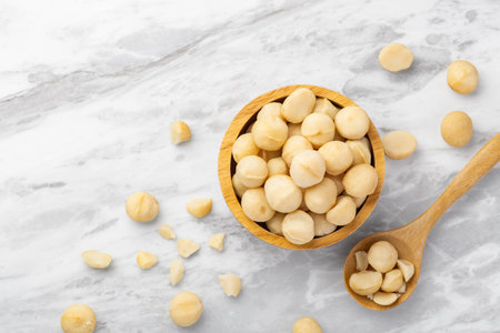 Macadamia nuts in wooden bowl with spoon and cracked macadamia on marble kitchen countertop background, top view, copy spaceの写真素材