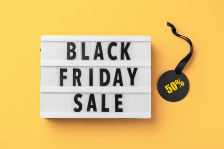 Lightbox with black friday sale word and discount tag with black ribbon on yellow background, top...