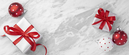 Christmas festive holiday background, white silver gift box with red bow ribbon and xmas ball decor on white marble table background, top view, copy spaceの写真素材
