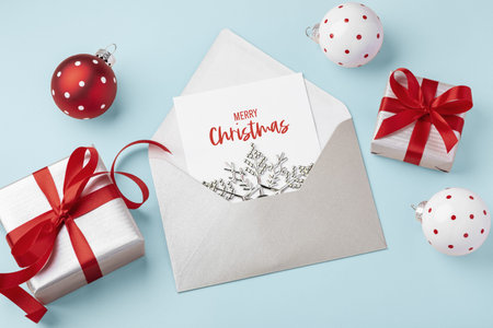 Merry Christmas holiday card in envelope and present gift boxes and xmas ball ornament on light blue...