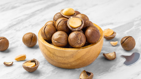 Macadamia nuts with shell in wood bowl with cracked macadamia  and tool on marble table, close upの写真素材