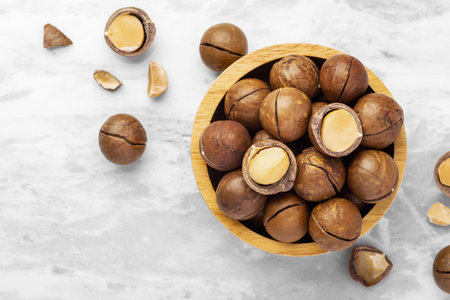 Macadamia nuts with shell in wood bowl and cracked macadamia on marble table background, top view, copy spaceの写真素材