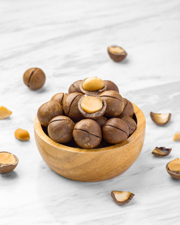 Macadamia nuts with shell in wood bowl with broken macadamia on marble table background, copy spaceの写真素材