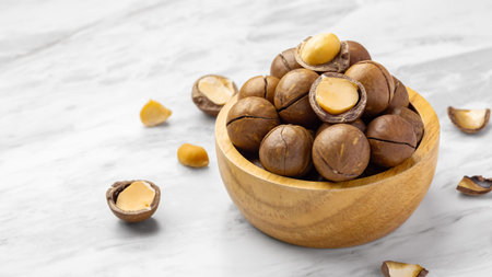 Macadamia nuts in wood bowl with broken macadamia on marble table background, closeup, copy space