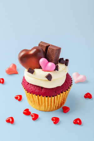 Valentines day red cupcake decorated with heart chocolate and pink hearts on blue background, celebrating love concept, copy spaceの写真素材