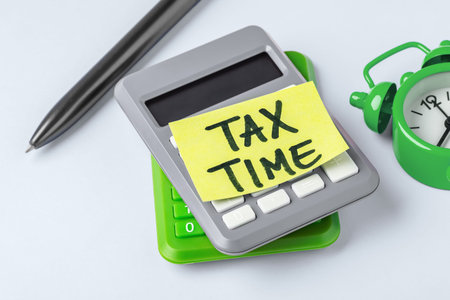 Reminder for tax payment, Calculator and Tax Time message on sticky note with pen and clock on white backgroundの写真素材