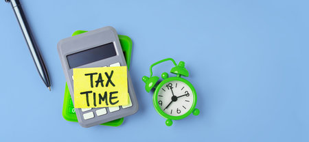 Tax time concept with calculator, alarm clock and sticky note on calculators on blue background, Financial planning and tax return deadline, flat lay, copy spaceの写真素材